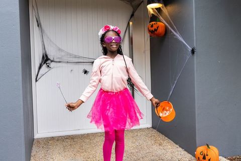 African american girl wearing pink tutu celebrating halloween on porch holding pumpkin