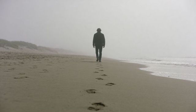 Solitary figure walking along foggy beach leaving footprints on misty shoreline