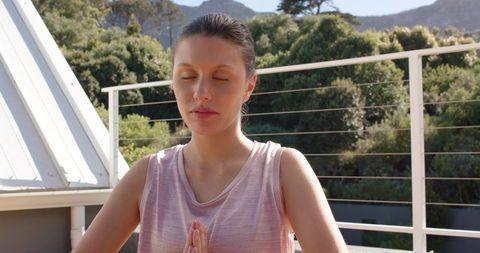Young woman meditating on balcony practicing mindfulness and prayer in sunlight