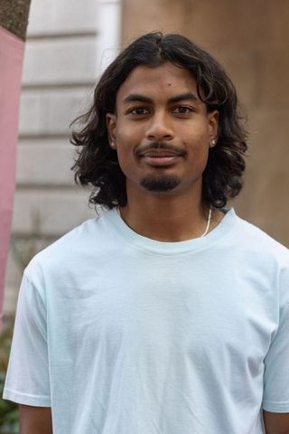 Indian man standing outdoors wearing light blue tee and silver jewelry, urban portrait
