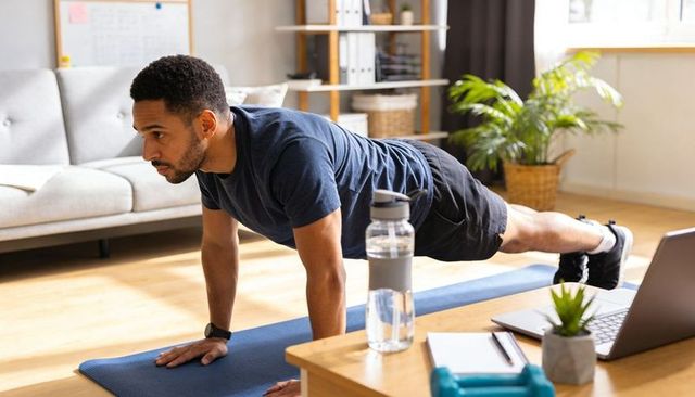 Man holding high plank on blue mat in bright living room during home workout