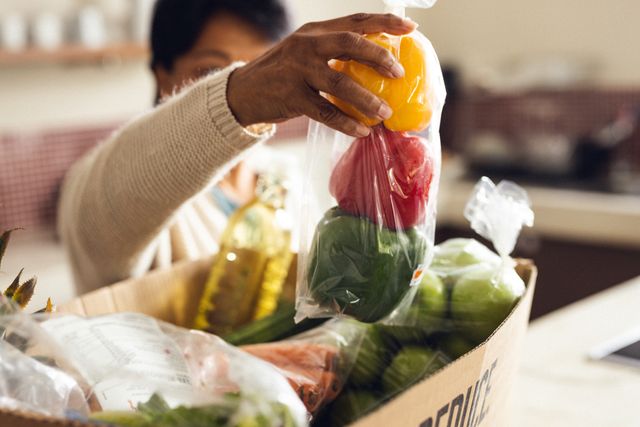 Hand of biracial mature woman unpacking fresh bell peppers from box in kitchen at home. Vegetable, groceries, food, shopping, unaltered, lifestyle and retirement concept.