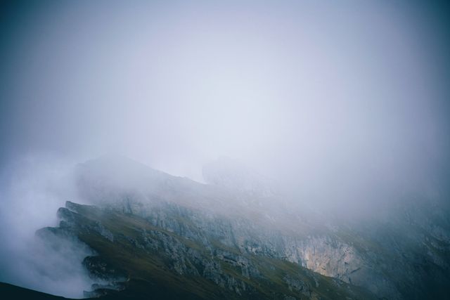 Misty mountain peaks shrouded in fog create an ethereal and tranquil atmosphere. Useful for nature blogs, travel articles, background images for websites, and inspirational content. Ideal for conveying a sense of mystery and peace.