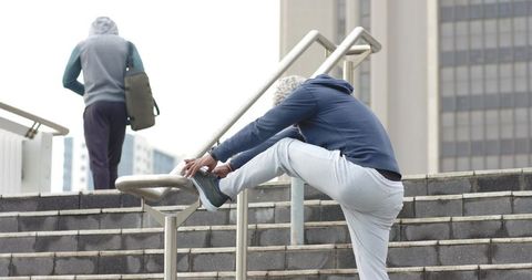 African American men walking city stairs, one stretching on handrail wearing hoodie and beanie