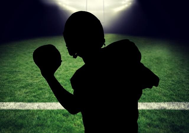 Rugby player silhouetted against an illuminated rugby field prepares to throw the ball at night. Ideal for advertisements and promotional materials for sports events, rugby tournaments, athletic training programs, and fitness campaigns that emphasize determination and dynamic action.