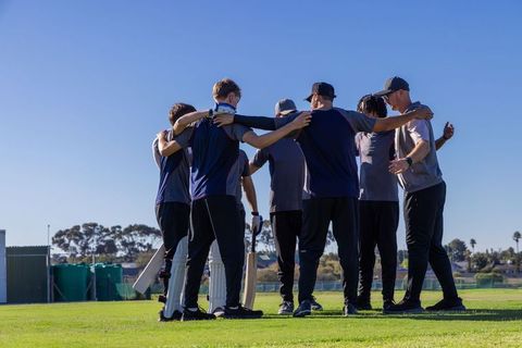 Cricket team huddling on sunny field before match with coach, bats pads and teamwork