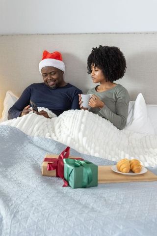 African-american couple relaxing in cozy bed with santa hat, coffee and christmas gifts