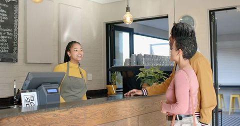 Smiling barista serving couple at modern cafe counter with qr code payment
