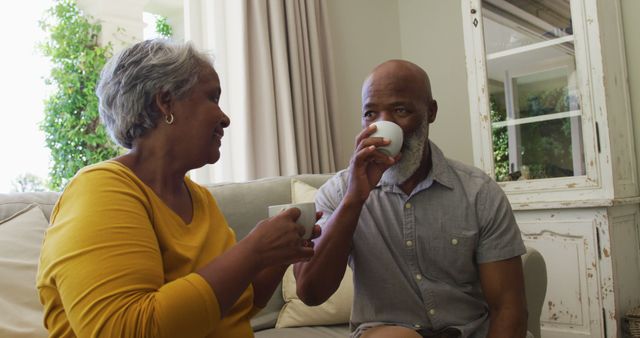African american senior couple smiling while having coffee together sitting on the couch at home. retirement senior couple lifestyle living concept