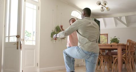 Father kneeling to welcome son at front door embracing in bright modern home