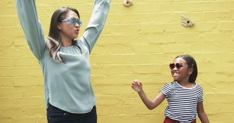 Joyful mother and daughter dancing near vibrant yellow wall