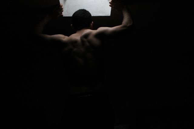 Muscular man training in a dimly lit space, showcasing his back muscles. Ideal for fitness motivation, workout advertisements, bodybuilding inspiration, and athletic lifestyle promotions.