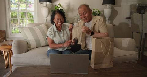 Smiling Senior Asian Couple Enjoys Online Shopping in Cozy Living Room
