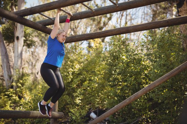 Woman participating in an outdoor obstacle course, demonstrating strength and determination while exercising on a monkey bar. Ideal for use in fitness, health, and lifestyle content, promoting physical activity and outdoor training.