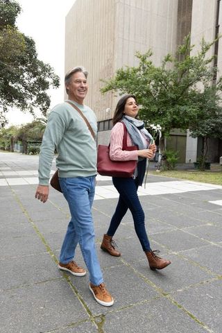 Middle-aged couple walking in urban plaza carrying flowers and red tote on casual stroll