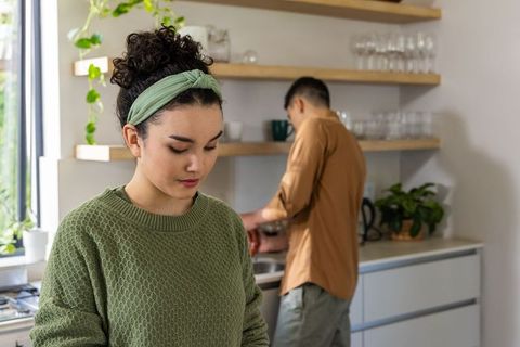 Asian couple preparing meal in modern kitchen with plants, wooden shelves and soft light