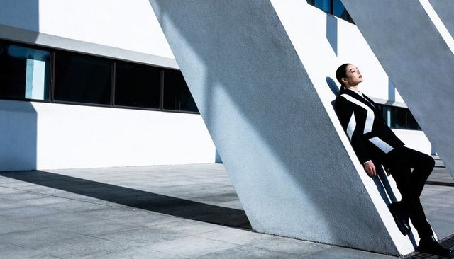 Leaning asian model posing against angled concrete column in geometric monochrome suit