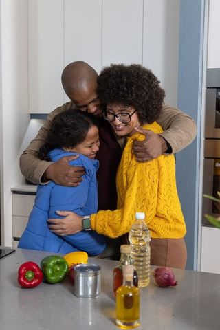 Family hugging around kitchen island with fresh peppers, cozy knitwear, joyful embrace