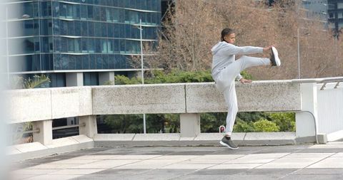 African american athlete stretching on urban barrier wearing grey tracksuit and sneakers