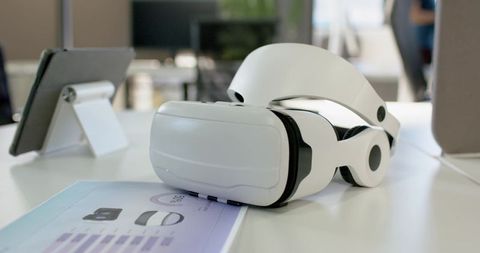 Sleek white VR headset resting on glossy desk with tablet and brochure in modern office