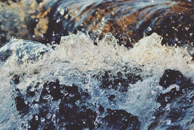 Close-up view of water splashing energetically on rocks in a natural river setting. Ideal for content related to nature, energy, and freshness. Perfect for use in environmental blogs, travel websites, and promotional material for outdoor activities.