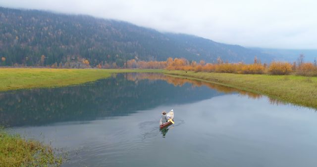 Calm river in autumn forest with misty mountains in background. Reflection of trees and sky is visible on water's surface. Ideal for promoting outdoor adventures, nature retreats, travel destinations, peaceful getaways, and camping trips.