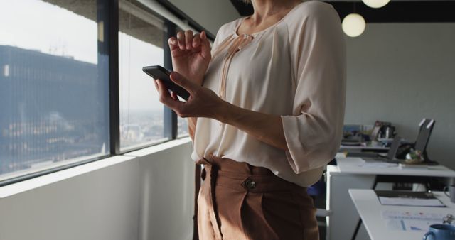 Businesswoman texting on smartphone while standing in office - Download Free Stock Images Pikwizard.com