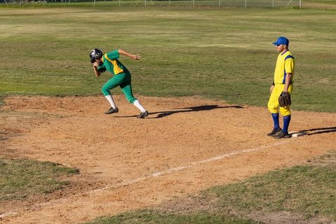 Baseball runner lunging off base while fielder watches during youth league game action