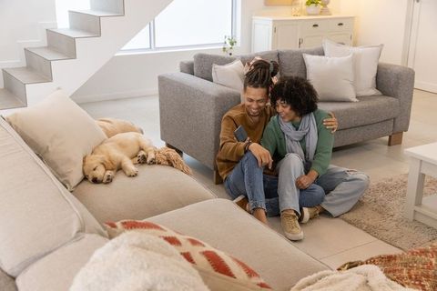Couple relaxing on living room floor with sleeping puppy, sharing phone and laughing