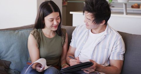 Young couple reviewing finances on sofa with tablet and documents