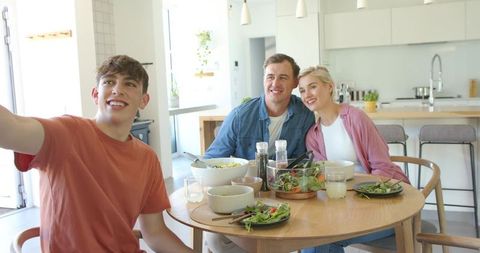 Sunlit family taking selfie at dining table with healthy salad, parents and teen