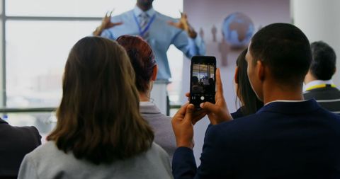 Business seminar speaker with attendee recording presentation