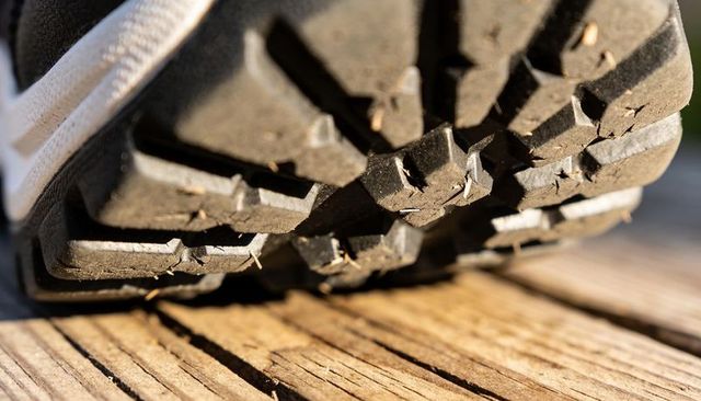 Macro rugged sneaker sole pressing onto wooden deck trapping dirt and grass