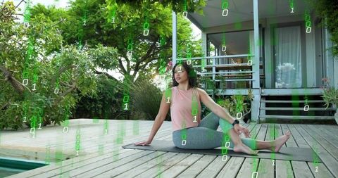 Woman Practicing Yoga Twist on Wooden Deck with Smartwatch and Digital Binary Overlay