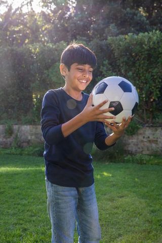 Joyful Boy Holding Soccer Ball on Sunlit Lawn