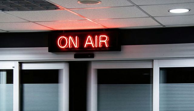 Glowing red on air neon sign casting warm light over broadcast studio glass corridor doors
