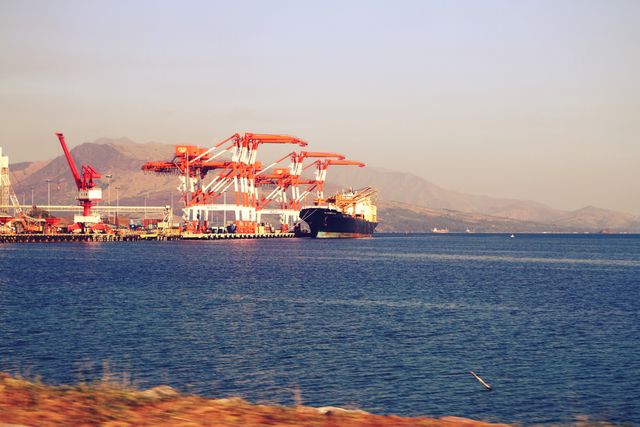 Cargo ship docked at a busy industrial port with large cranes loading and unloading shipping containers. Suitable for themes such as logistics, international trade, maritime transportation, business, and industrial infrastructure.