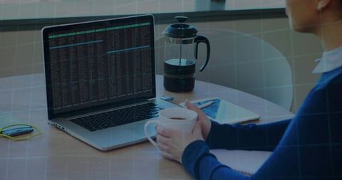 Remote developer holding coffee while viewing terminal on laptop at home workspace