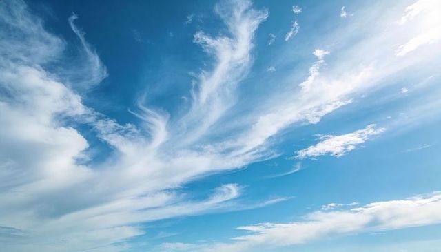 Expansive blue sky with wispy cirrus clouds and sun glow over horizon background