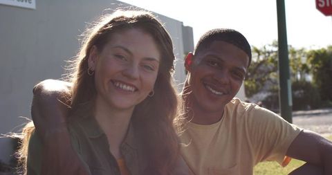 Young couple smiling and embracing on sunlit urban street conveying warmth and friendship