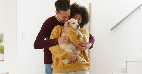 Multiracial couple cuddling light-colored puppy in cozy modern home