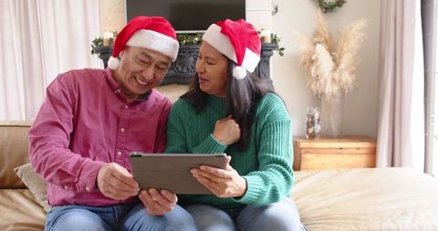 Couple Wearing Santa Hats Using Tablet in Festive Living Room