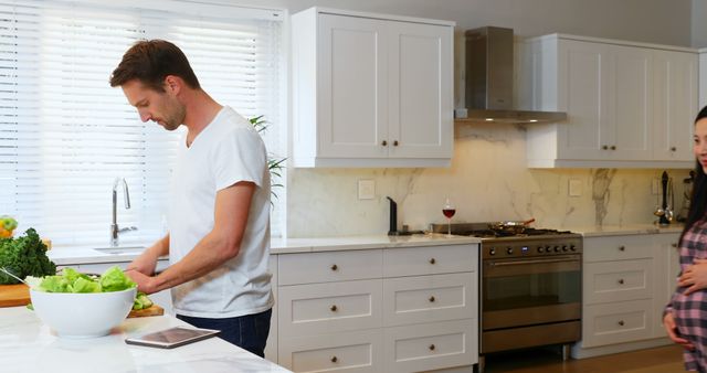 Husband Preparing Salad in Modern Kitchen with Pregnant Wife Observing - Download Free Stock Images Pikwizard.com