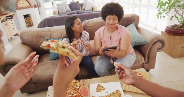 Family sitting on a cozy sofa eating pizza in a comfortable living room. Everyone is engaged in conversation and enjoying their time together. Can be used for ads or articles about family bonding, casual dining, or comfortable home living.