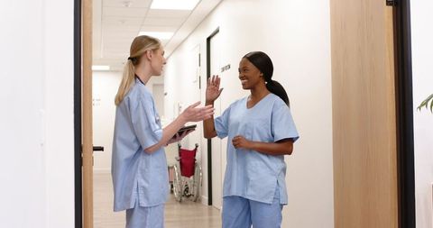 Diverse Nurses High-Fiving in Clinic Corridor Celebrating Teamwork and Patient Care