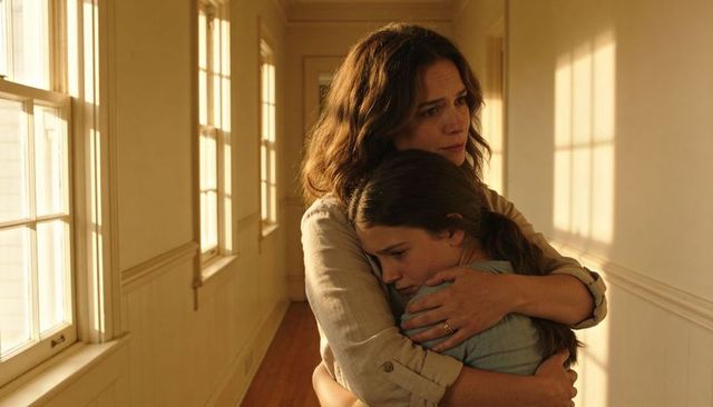 Mother and daughter embracing in sunlit hallway, protective hug showing warmth