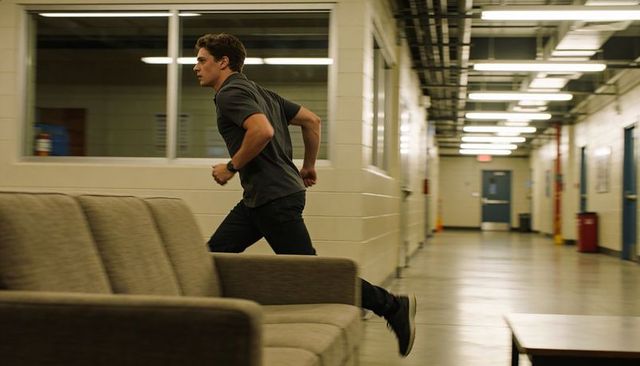Young man running through dim corridor past sofa window wearing dark polo and sneakers