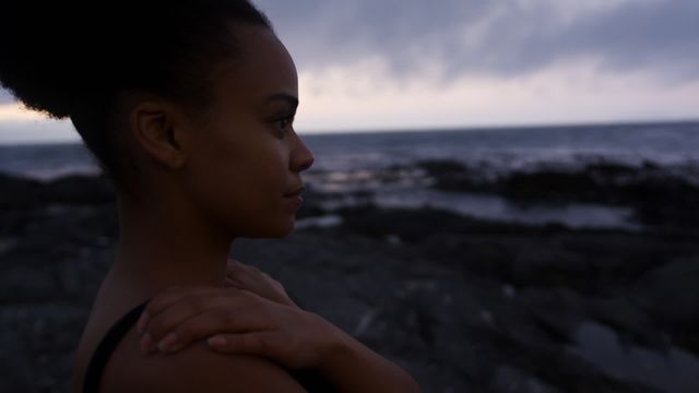 Side view of an athletic woman pausing during her workout to enjoy the seaside landscape. Ideal for concepts related to fitness, wellness, nature, self-reflection, and outdoor activities.