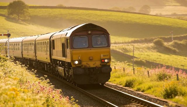 Diesel locomotive running through sunlit countryside with wildflowers and semaphore