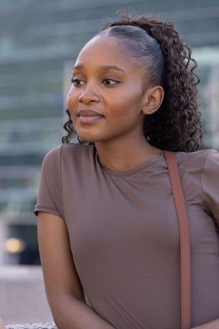 Confident african woman standing in urban plaza wearing brown fitted top and crossbody bag